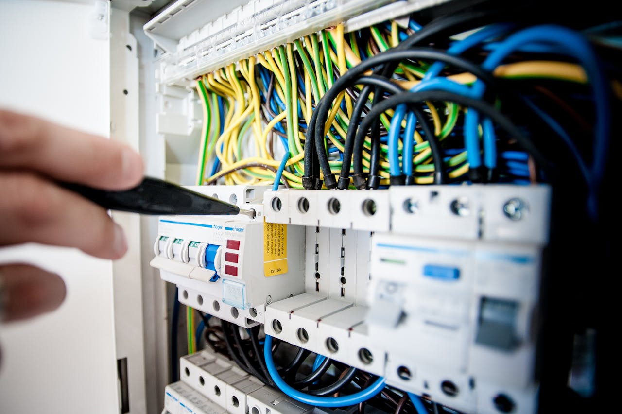 services-03 Hand of electrician working on a circuit breaker panel with colorful wires, ensuring safe electrical connections.