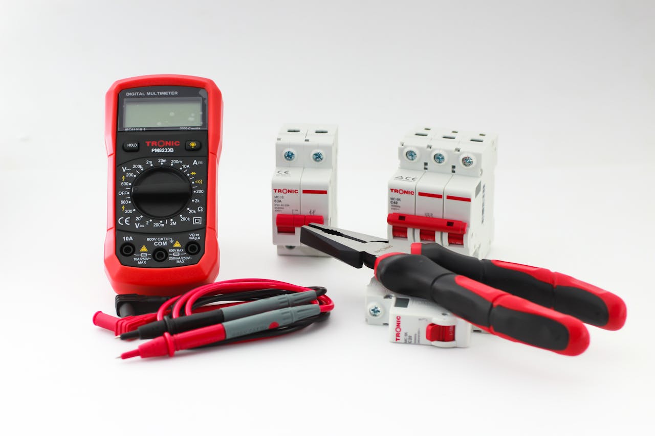 why-choose-us Close-up of a digital multimeter with electrical tools and circuit breakers on a white background.