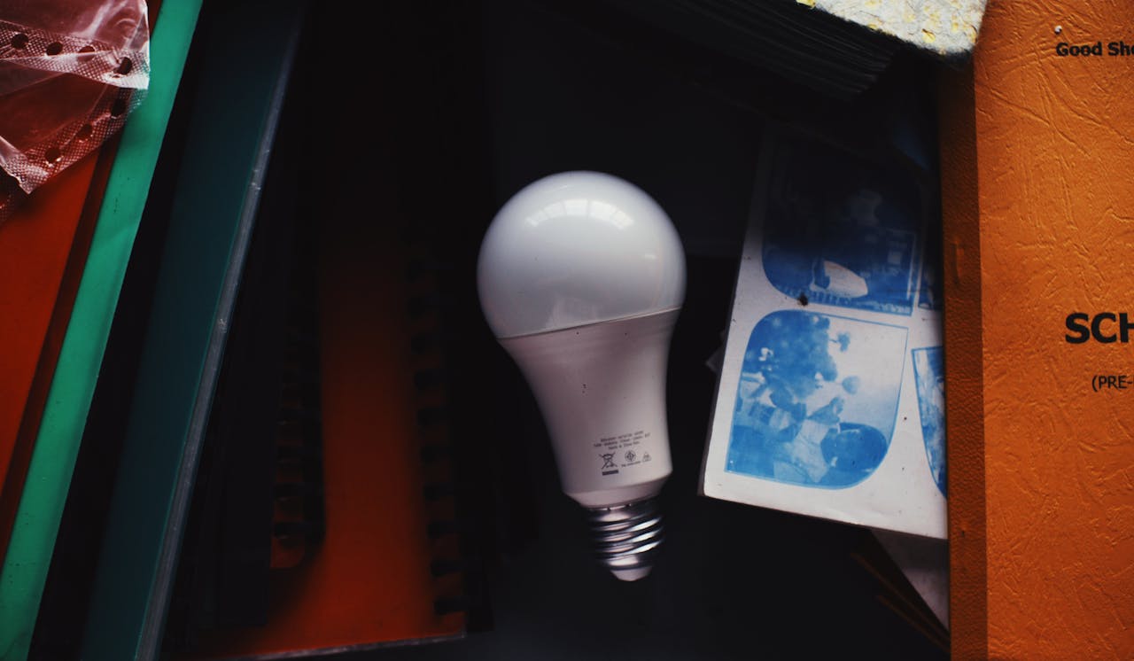 services-01 A LED bulb placed among books, color prints, and papers inside a home, showcasing a study environment.